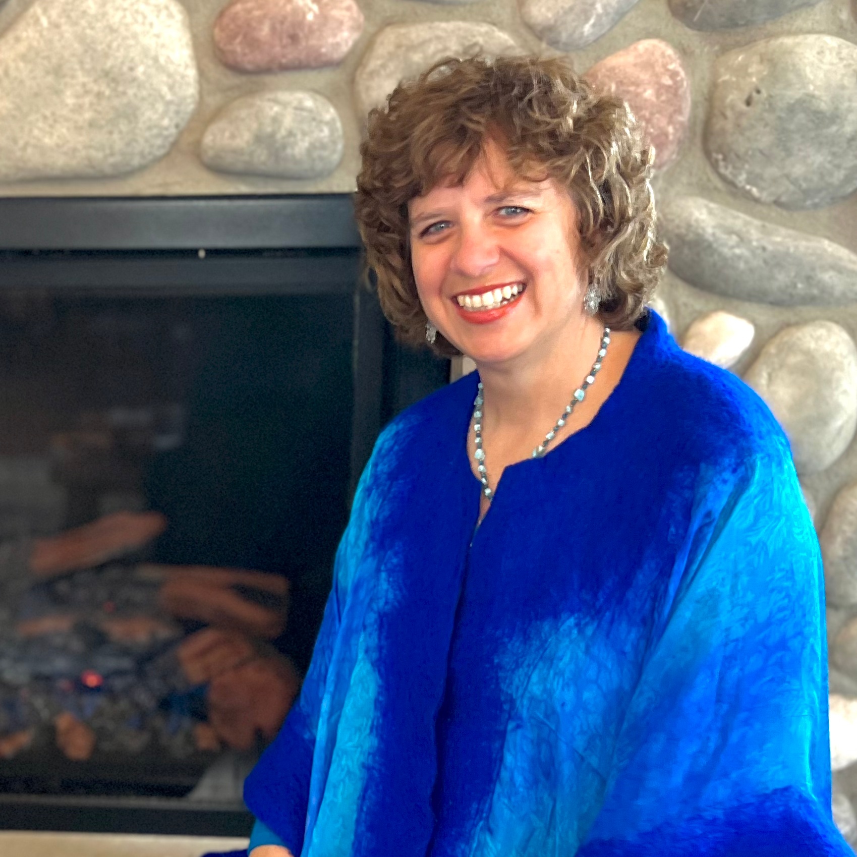 Sarah DeVoe smiling in a blue top in front of a stone fireplace